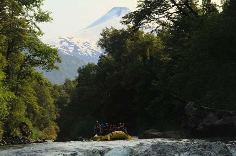 Rafting in Chile on river in deep forest and volcano in background, photo by Next Level of Travel