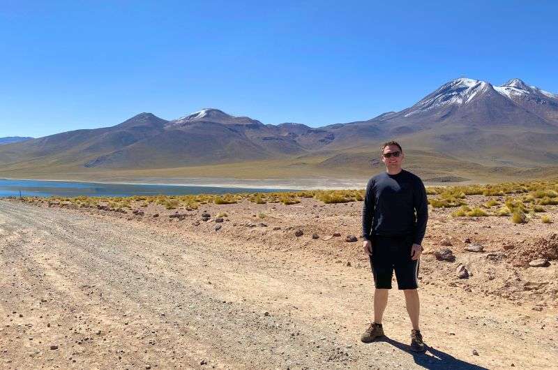 Traveler on dirt road near body of water and snow-capped mountains, exploring Chile in 3 weeks, photo by Next Level of Travel