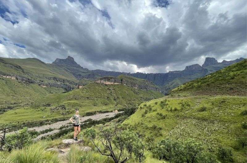 A woman hiking Tugela Gorge with the Amphitheatre in the background, Drakensberg South Africa