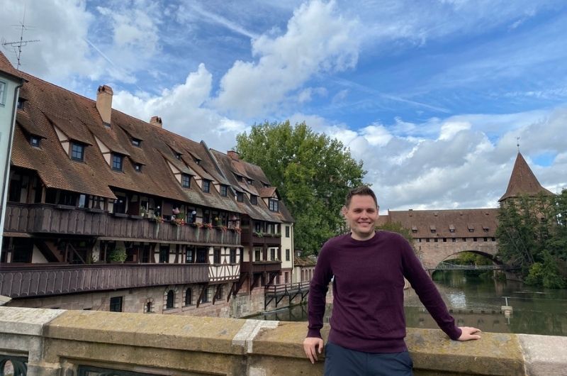 Tourist on bridge in Nuremburg with historical buildings and river in background, photo by Next Level of Travel 