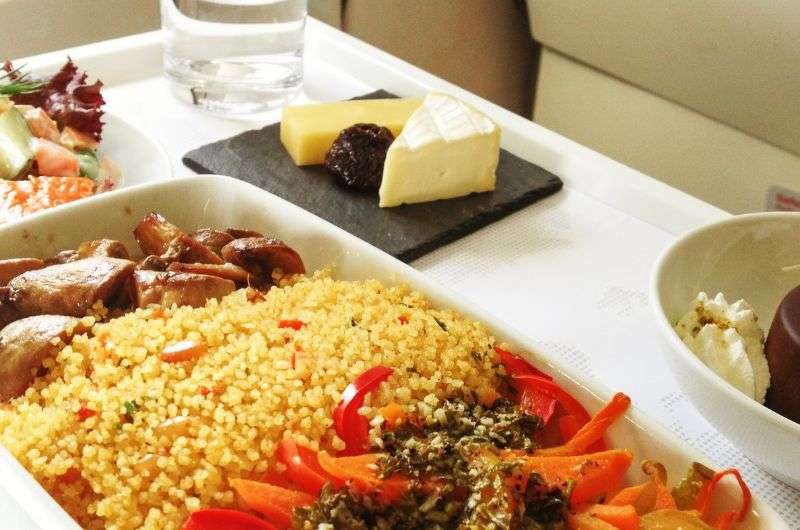 A gourmet in-flight meal featuring couscous, vegetables, chicken, cheese, and dessert