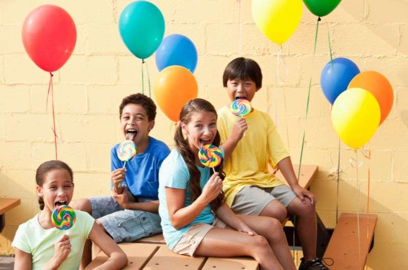 Kids sitting on the bench, eating lollipops. 